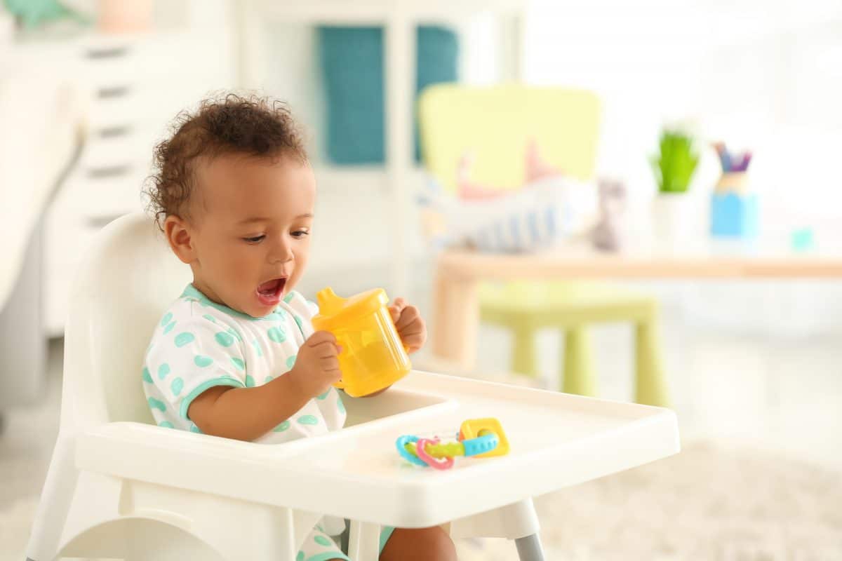Baby holding orange cup in a high chair