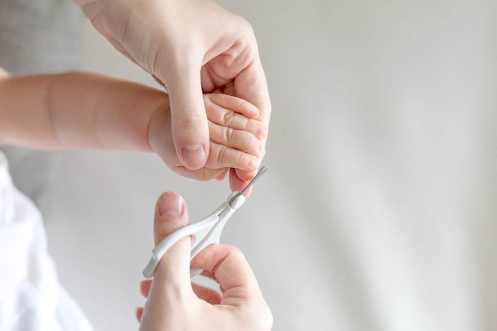 Close up of parent cutting baby’s nails with scissors