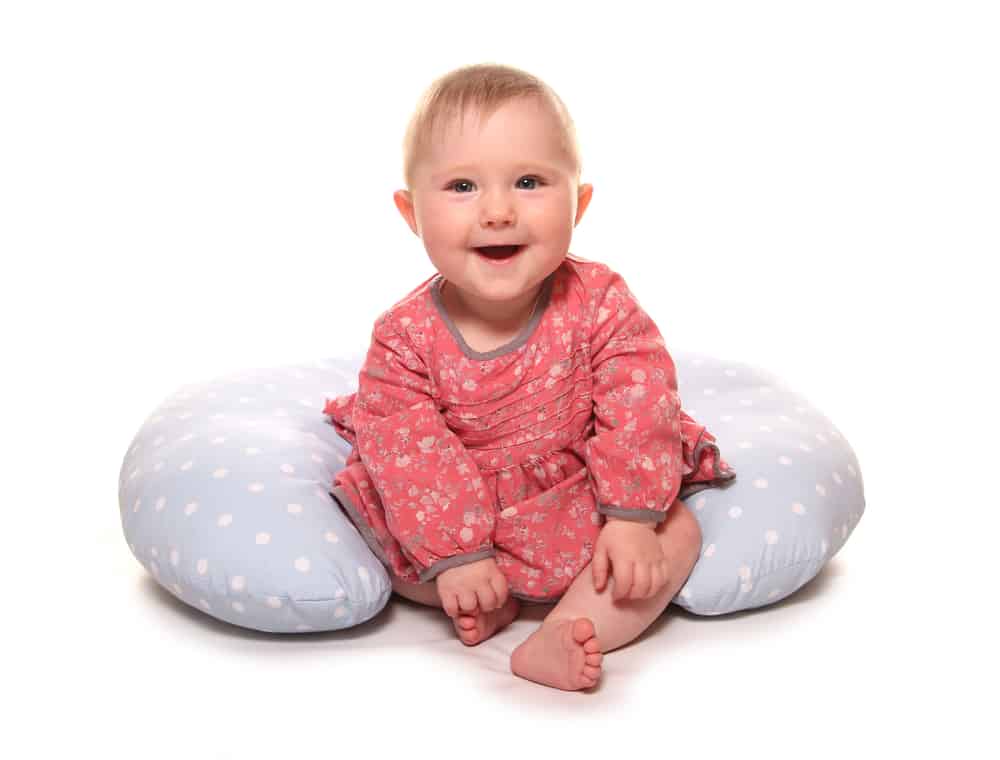 Happy baby boy sitting in front of a u-shape nursing pillow