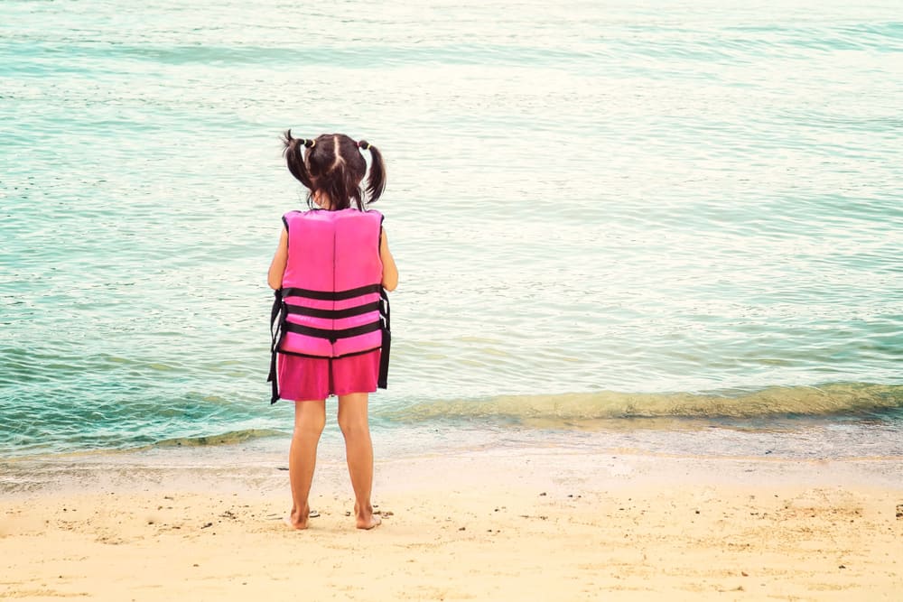 child standing on beach wearing life jacket