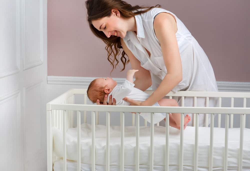 smiling mother putting her child in the crib