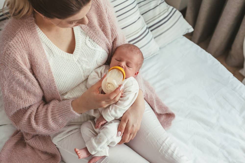 mother bottle feeds newborn baby on bed