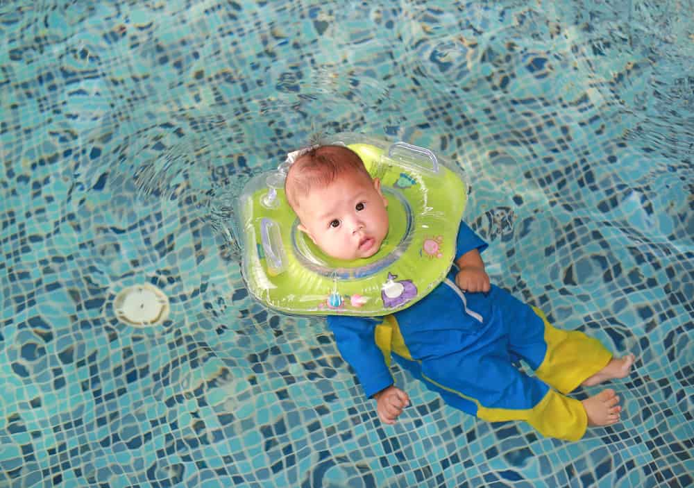 baby in pool wearing green inflatable neck float