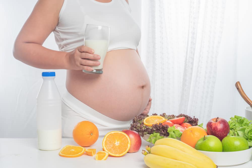 pregnant woman holding milk near healthy foods
