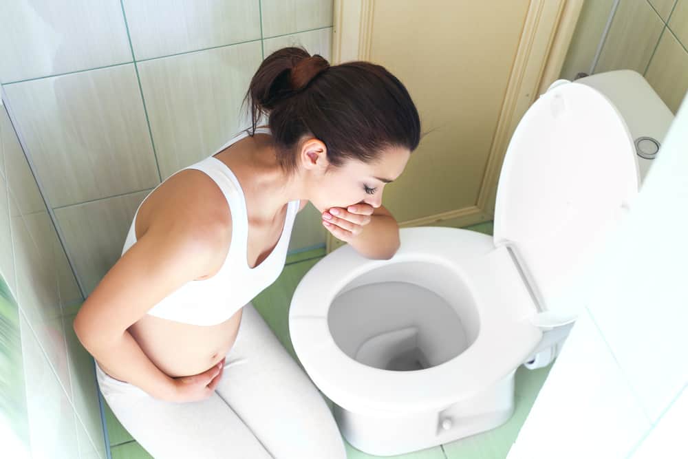 a pregnant woman feeling sick and leaning over the toilet