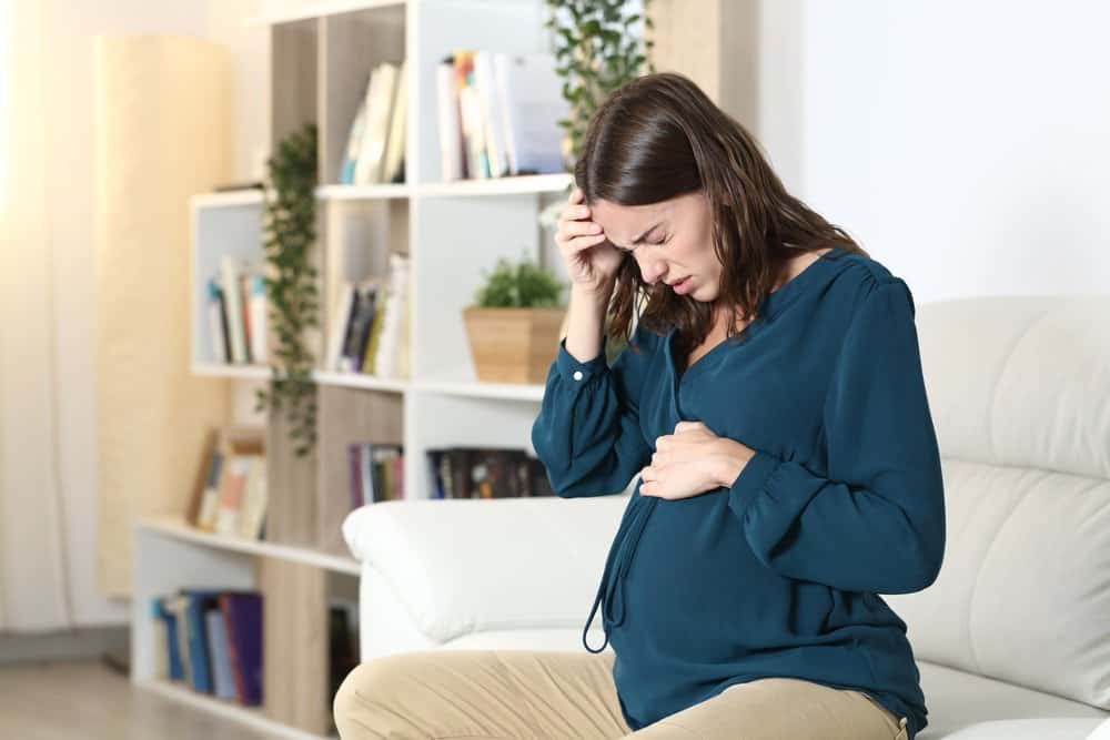a pregnant woman sitting on the couch and in pain