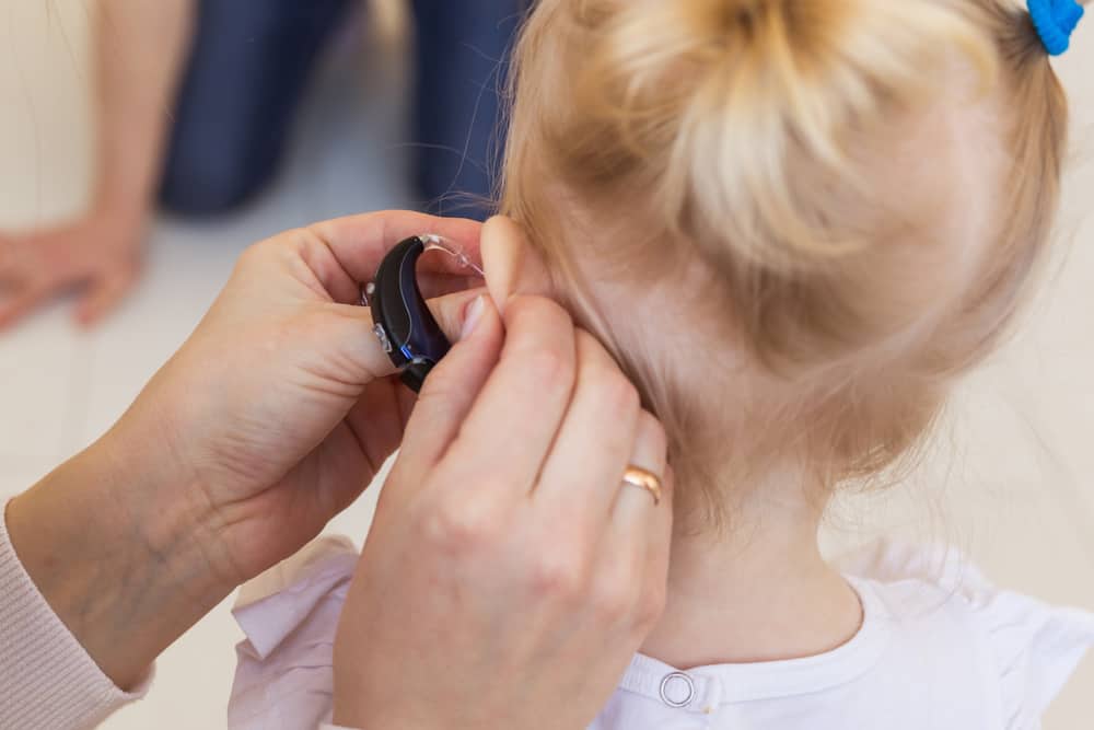 mother putting hearing aid on girl toddler