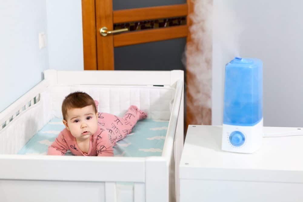 a baby in a crib with a humidifier working on the counter next to him