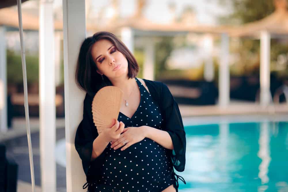 a pregnant woman by a pool wearing a swimsuit and suffering from the heat