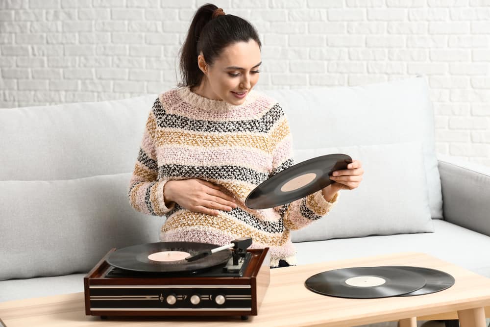 a pregnant woman chooses a record to listen to with her record player