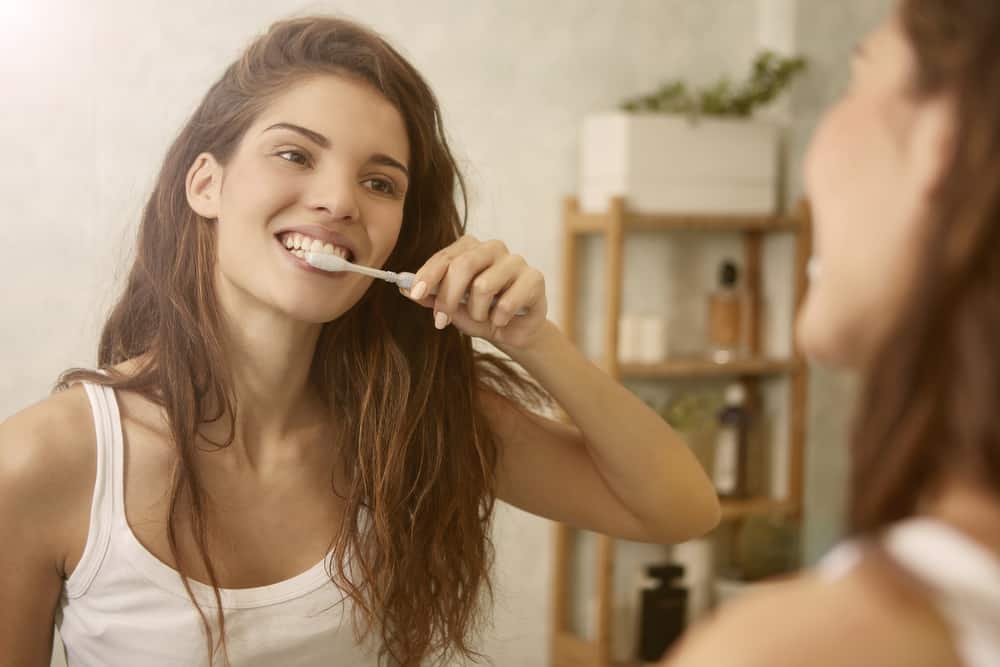 a woman looks in the mirror while brushing her teeth