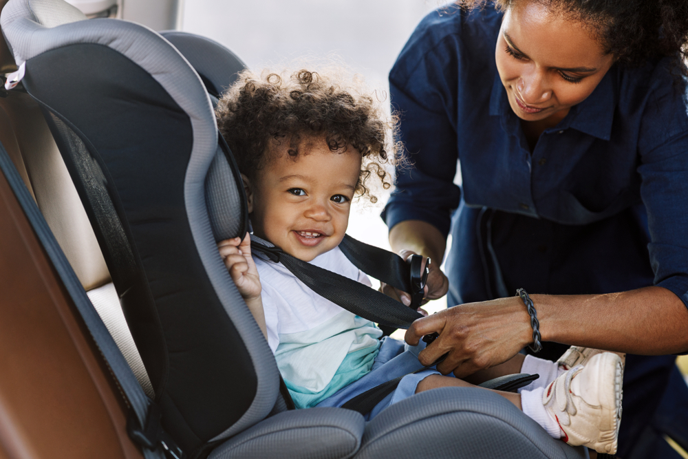 Woman straps a smiling baby into a booster seat